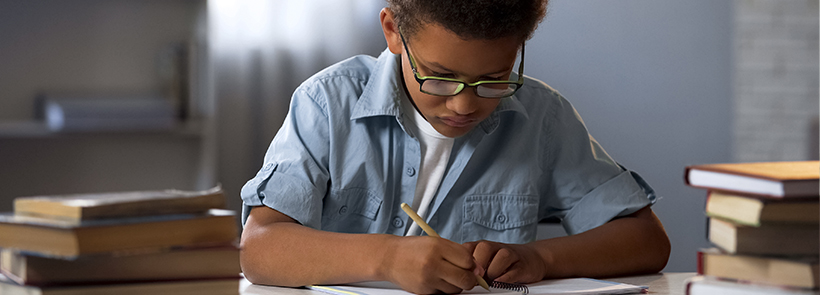 child writing surrounded by books